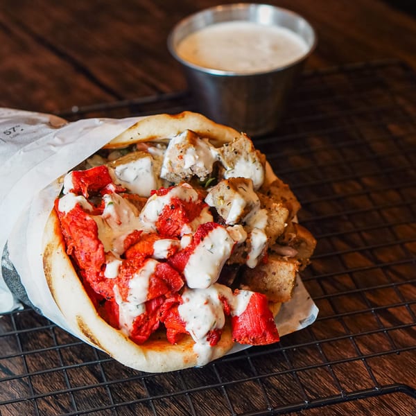 Haazs halal gyro with red and white meat, drizzled with white sauce, next to a sauce cup.
