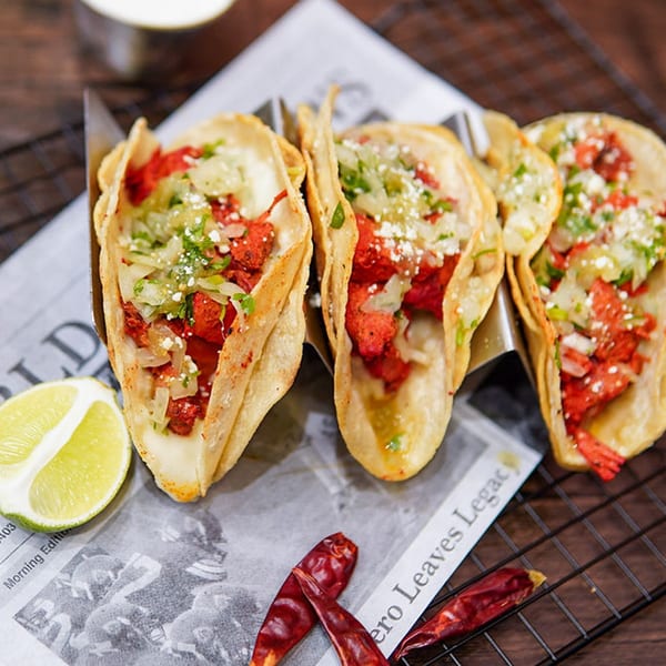 Three Haazs halal tacos with red meat, onions, and cheese, served with lime and dried chilies.