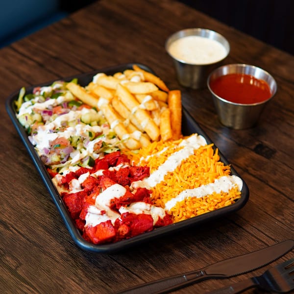 Haazs halal platter with red chicken, yellow rice, fries, salad, and white sauce, with two dipping sauces.