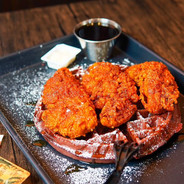 Haazs' halal chicken and waffles, with crispy fried chicken pieces on a dark waffle, dusted with powdered sugar.